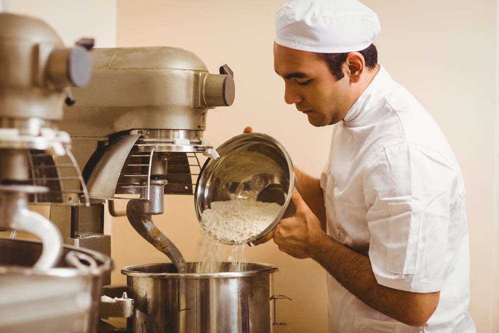baker pouring flour into a large mixer